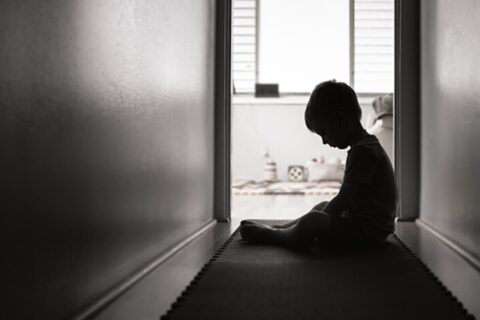 Child sadly sitting in dark hallway